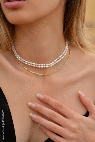 Close-up of a beautiful young blonde woman's neck  with gold earrings and pearl,  gold and diamonds necklaces