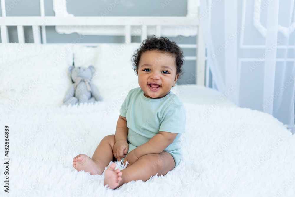 African-American baby smiles or laughs while sitting on the bed at home African-American baby smiles or laughs while sitting on the bed at home