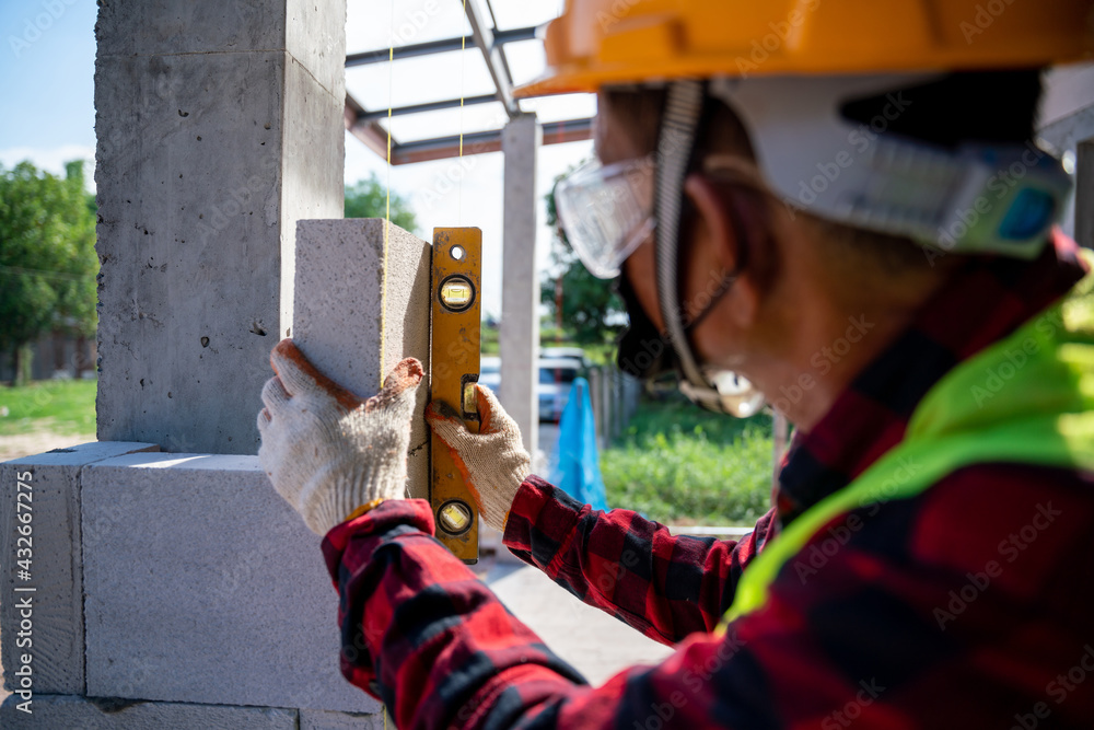Close-up bricklayer builder using the water level, check the inclination of autoclaved aerated concrete blocks. Walling, installing bricks on construction site Close-up bricklayer builder using the water level, check the inclination of autoclaved aerated concrete blocks. Walling, installing bricks on construction site