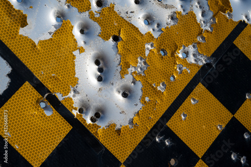 Photography Close-up of checkered road sign with bullet and shotgun holes.