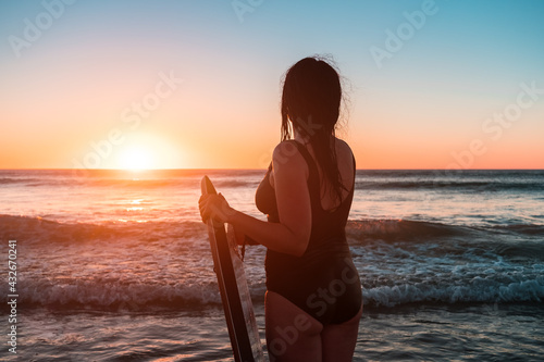 Woman with bodyboard entering the ocean at sunset, Moana Beach, South Australia photo