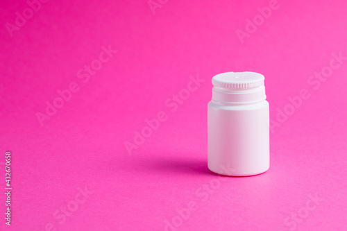 White jar of pills or vitamins on a pink paper background. Medicine on background with copy space.