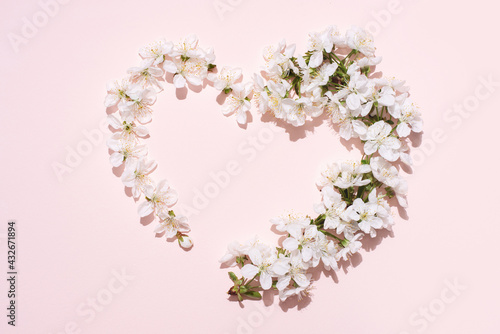 White cherry flowers in the shape of a heart on a pink background in bright sunlight, love, wedding, spring concept.