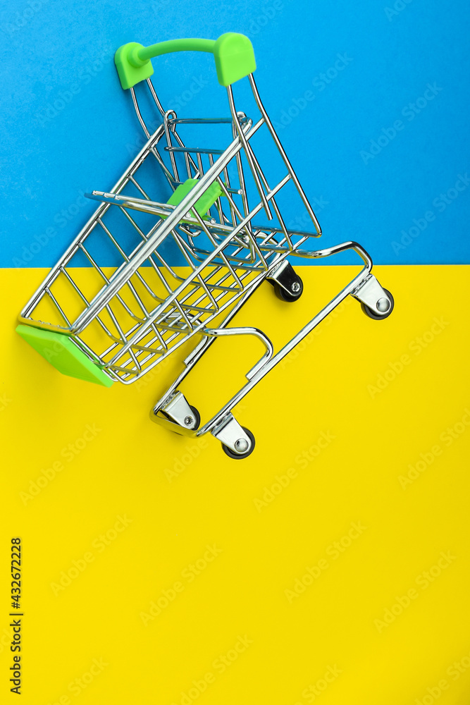 Empty shopping cart isolated on yellow and blue background, grocery cart dropped. Supermarket food price. Colors of the Ukrainian flag. Ukrainian financial crisis. Selective focus, copy space. Empty shopping cart isolated on yellow and blue background, grocery cart dropped. Supermarket food price. Colors of the Ukrainian flag. Ukrainian financial crisis. Selective focus, copy space.