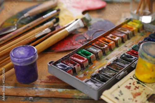 Different paints and brushes on wooden table, closeup