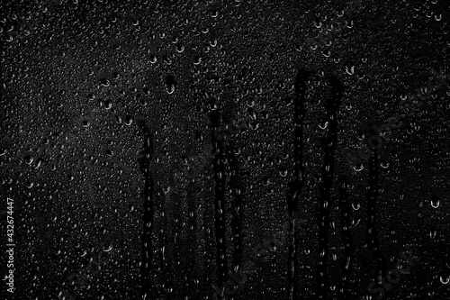 Drops of water flow down the surface of the clear glass on a black background. Texture for creativity. photo