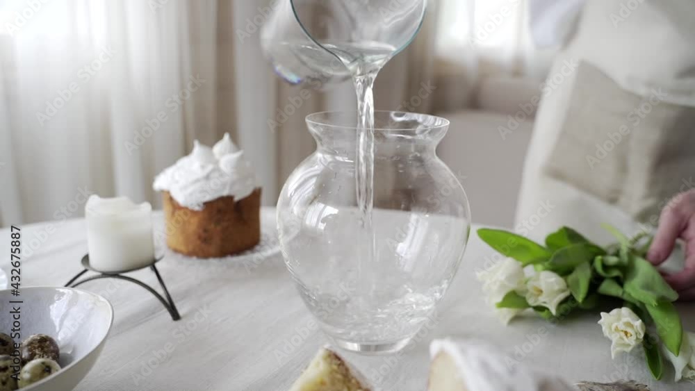 Young woman pours water from a glass decanter into a glass vase Young woman pours water from a glass decanter into a glass vase