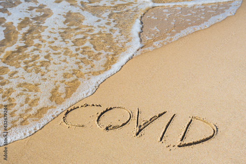 Covid written on the sand of a beach with wave washing the word, erasing or canceling it during Coronavirus summer, Covid free, safe beach, vaccine. Covid-19 immunity passport or pass, bathing season