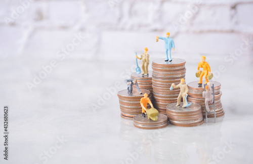 Selective focus engineering people and architecture miniature workers team working standing on stack of coin, with blue background.Team work financial business and construction success concept. photo