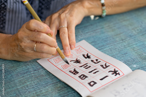 close up hands of senior woman practices eriting calligraphy of traditional chinese characters (focus at tip of brush) photo