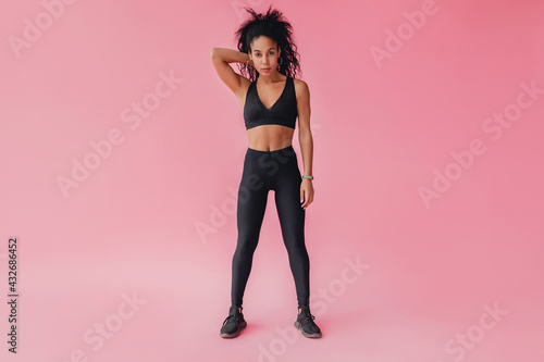 Fototapeta Naklejka Na Ścianę i Meble -  attractive black african american woman in black leggins fitness outfit on pink background