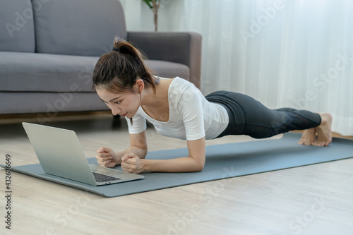 Fit, sporty asian young beautiful woman, girl doing yoga pose planking, watching trainer online on laptop computer, training in living room. Workout fitness exercise people in sportswear at home.