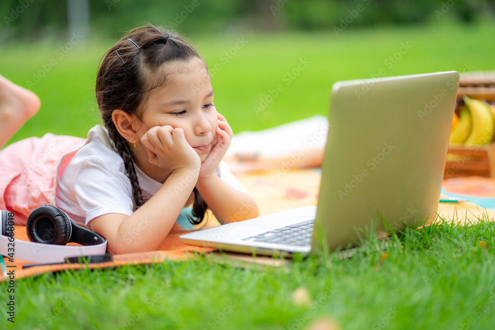Little girl laying down with tablet sitting in the park. School child resting outdoors. Little girl laying down with tablet sitting in the park. School child resting outdoors.