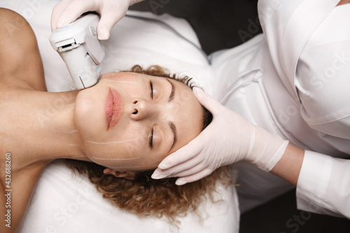 Spa salon and hardware cosmetology. SMAS non surgical ultrasound facelift procedure carried out by beautician dermatologist in beauty clinic. Ultrasonic device produce collagen on client face skin