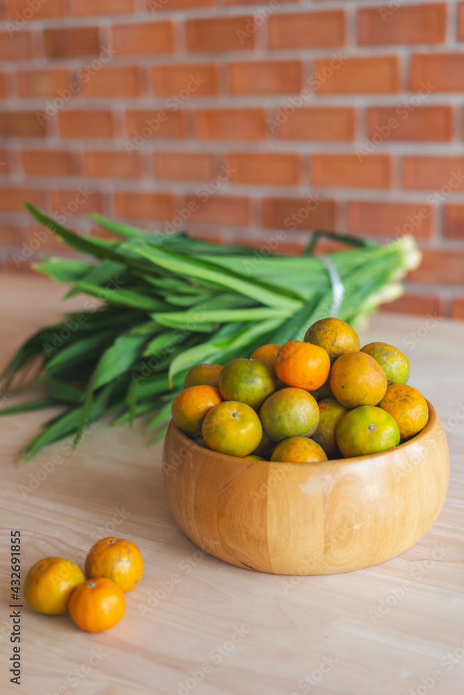 Fresh orange in the wooden bowl put on the wooden table with the pandanus behind. Orange is a healthy fruit and have refreshing sweet taste.