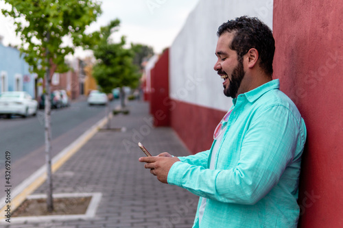Young bearded mexican man wearing a blue dress shirt smiling as he looks at his smartphone in the magic town of Cholula, Mexico
