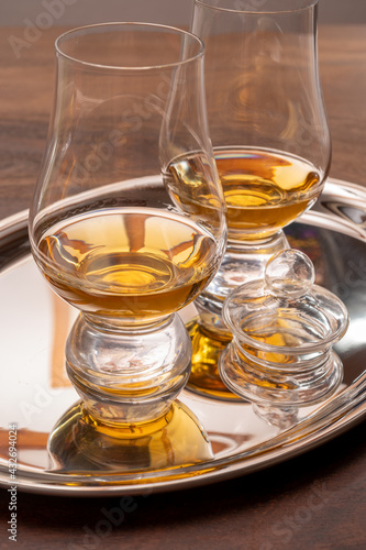 Tasting glasses of single malt scotch whisky served on steel mirror tray with reflection