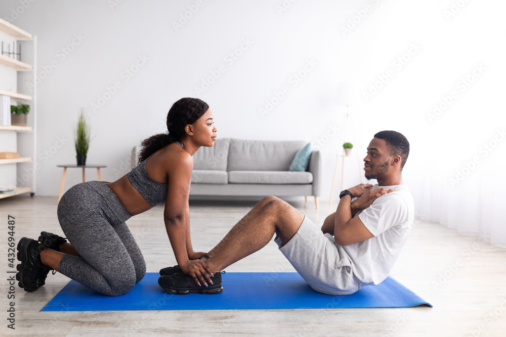 Millennial black guy doing abs exercises with his girlfriend, training as team at home, side view Millennial black guy doing abs exercises with his girlfriend, training as team at home, side view