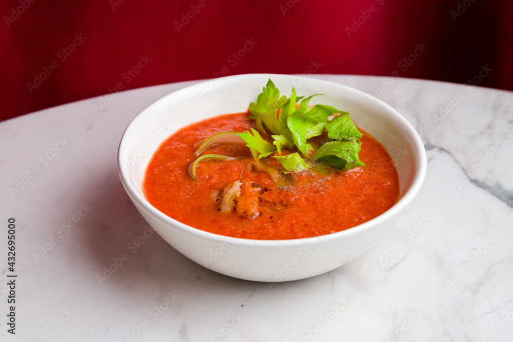 Soup cream of tomato with shrimps and greens on marble table with red curtain back Soup cream of tomato with shrimps and greens on marble table with red curtain back
