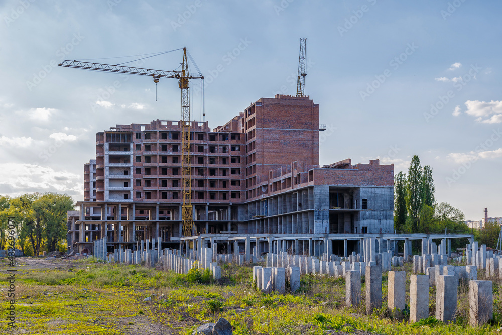 Tall building under construction with scaffolds,Freestanding tower crane on a building site.Building construction site work against blue sky Tall building under construction with scaffolds,Freestanding tower crane on a building site.Building construction site work against blue sky