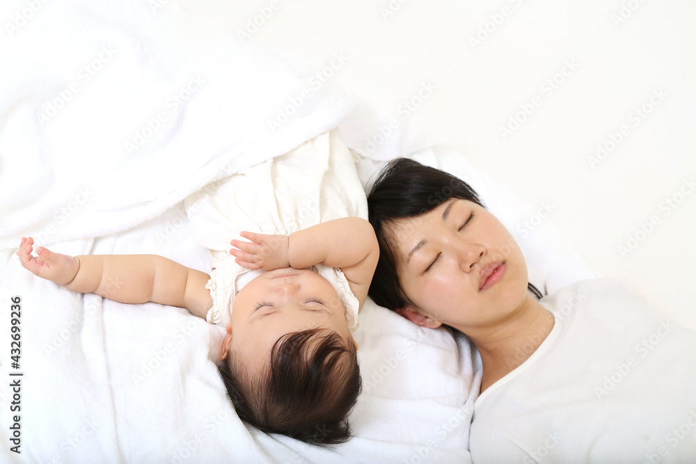 Mom taking a nap with her baby on a background of white sheets Mom taking a nap with her baby on a background of white sheets