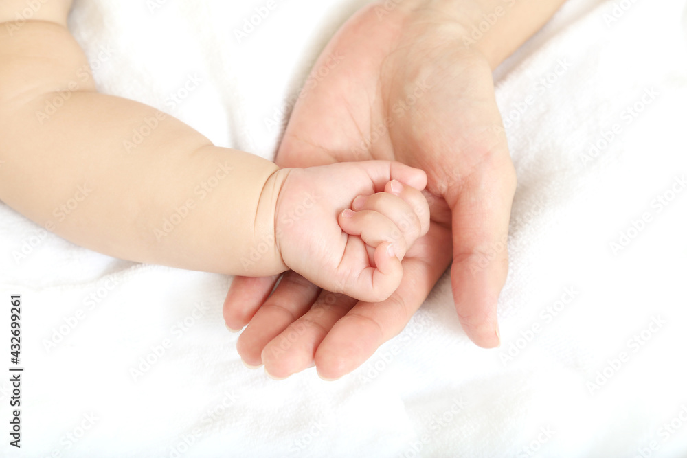 Baby little hand on mom's hand against white sheets background Baby little hand on mom's hand against white sheets background