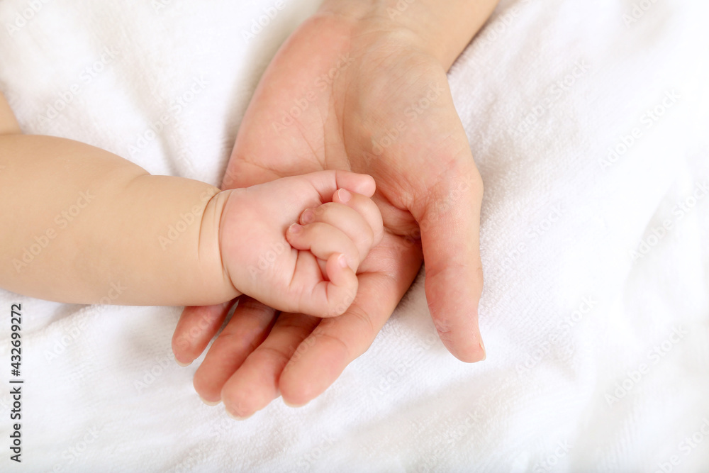 Baby little hand on mom's hand against white sheets background Baby little hand on mom's hand against white sheets background