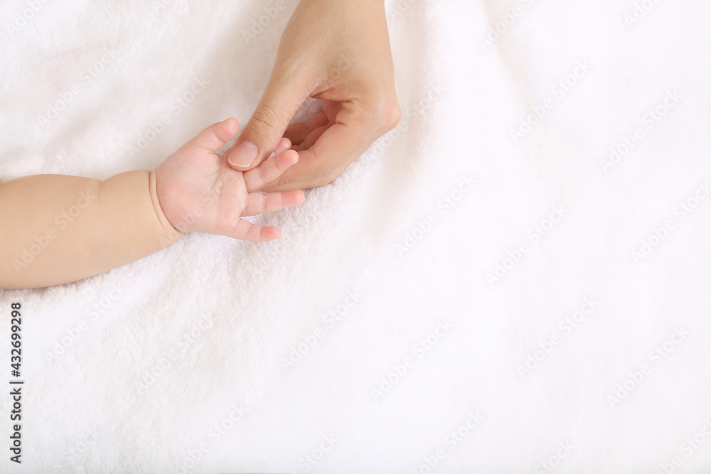 Mother's hand gently touching baby's hand on white sheets Mother's hand gently touching baby's hand on white sheets