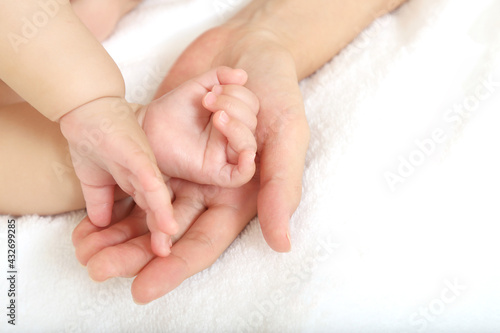 Baby little hand on mom's hand against white sheets background © chikala
