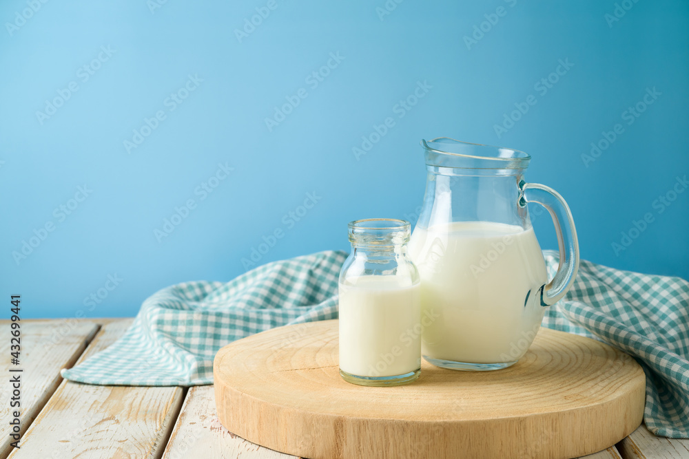 Milk jug and milk bottle on wooden table with tablecloth and log tray over blue background. Kitchen mock up for design Milk jug and milk bottle on wooden table with tablecloth and log tray over blue background. Kitchen mock up for design
