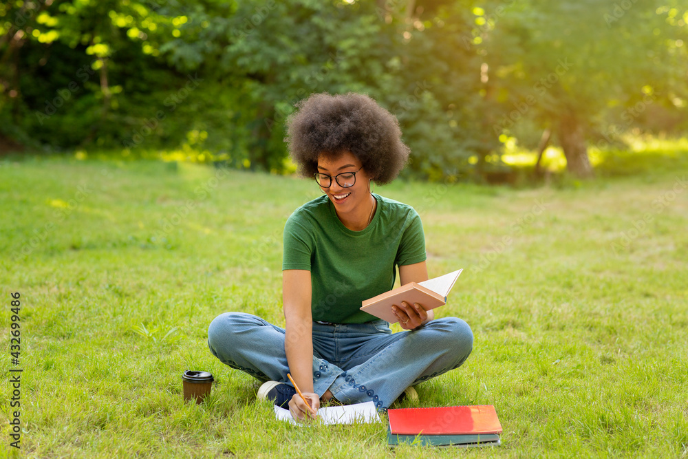 Cheerful African Student Girl Preparing Lessons Outdoors, Reading Book And Taking Notes