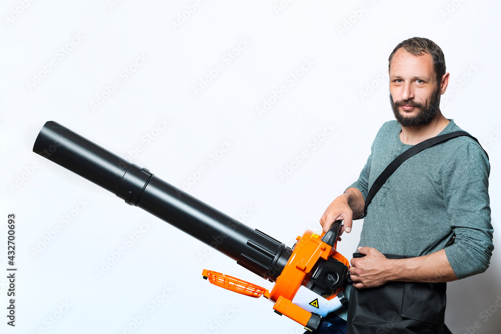 Handsome bearded man holding a Garden blower with a collection bag on gray background. Worker with a leaf blower with a bag. Leaf blower with dust filter bag. Handheld Blowing leaves away. Tools Handsome bearded man holding a Garden blower with a collection bag on gray background. Worker with a leaf blower with a bag. Leaf blower with dust filter bag. Handheld Blowing leaves away. Tools