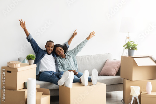 Happy Owners. Joyful Black Spouses Relaxing On Couch Among Boxes After Relocation