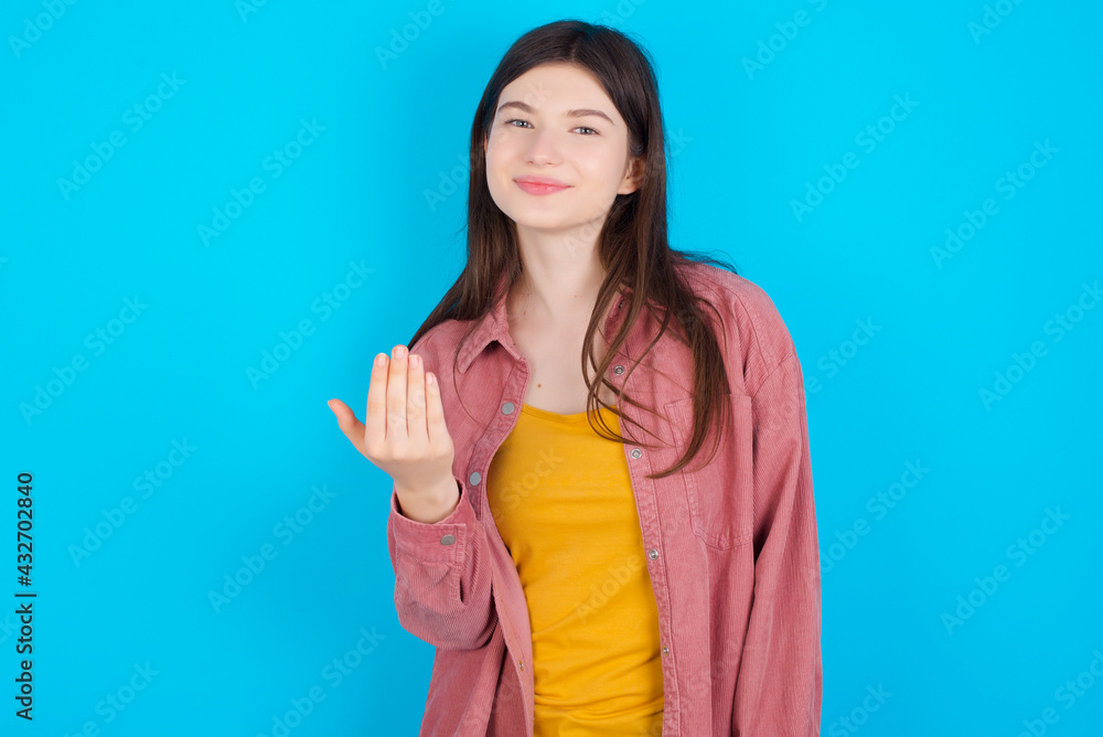 young beautiful Caucasian woman wearing pink jacket over blue wall, inviting you to come, confident and smiling making a gesture with hand, being positive and friendly. young beautiful Caucasian woman wearing pink jacket over blue wall, inviting you to come, confident and smiling making a gesture with hand, being positive and friendly.