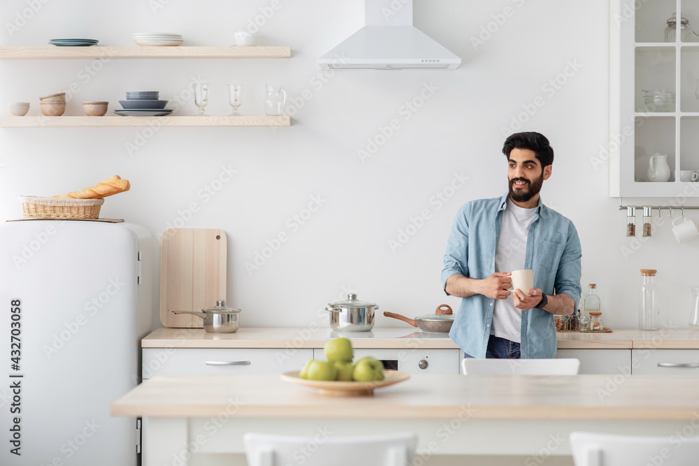 Harmony of life. Dreamy arab guy drinking coffee in the kitchen looking aside at window, enjoying hot drink Harmony of life. Dreamy arab guy drinking coffee in the kitchen looking aside at window, enjoying hot drink