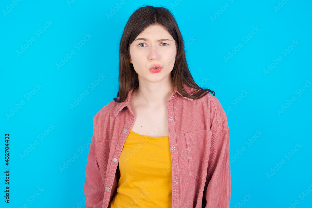 young beautiful Caucasian woman wearing pink jacket over blue wall expressing disgust, unwillingness, disregard having tensive look frowning face, looking indignant with something. young beautiful Caucasian woman wearing pink jacket over blue wall expressing disgust, unwillingness, disregard having tensive look frowning face, looking indignant with something.