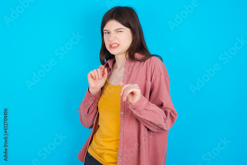 Ugh how disgusting! Displeased young beautiful Caucasian woman wearing pink jacket over blue wall, has dissatisfied facial expression as sees something abominable. photo