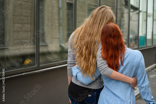 Same-sex relationships. A happy lesbian couple walked along the street and gently hug each other around the waist. The backs of two beautiful women on a date with a bouquet of dried flowers. LGBT.