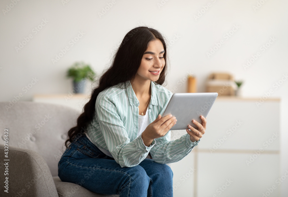 Cheerful Indian lady sitting in armchair with tablet computer, studying remotely or having online meeting at home Cheerful Indian lady sitting in armchair with tablet computer, studying remotely or having online meeting at home