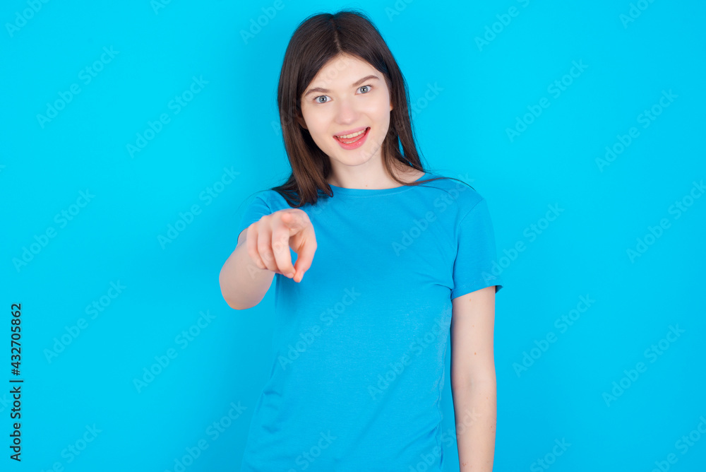 Excited positive young beautiful Caucasian woman wearing blue T-shirt over blue wall points index finger directly at you, sees something very funny. Wow, amazing Excited positive young beautiful Caucasian woman wearing blue T-shirt over blue wall points index finger directly at you, sees something very funny. Wow, amazing