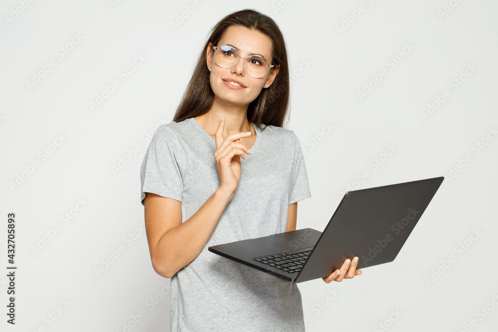 Beautiful student girl in casual clothes and glasses working on laptop. Working from home. Gray background. Beautiful student girl in casual clothes and glasses working on laptop. Working from home. Gray background.