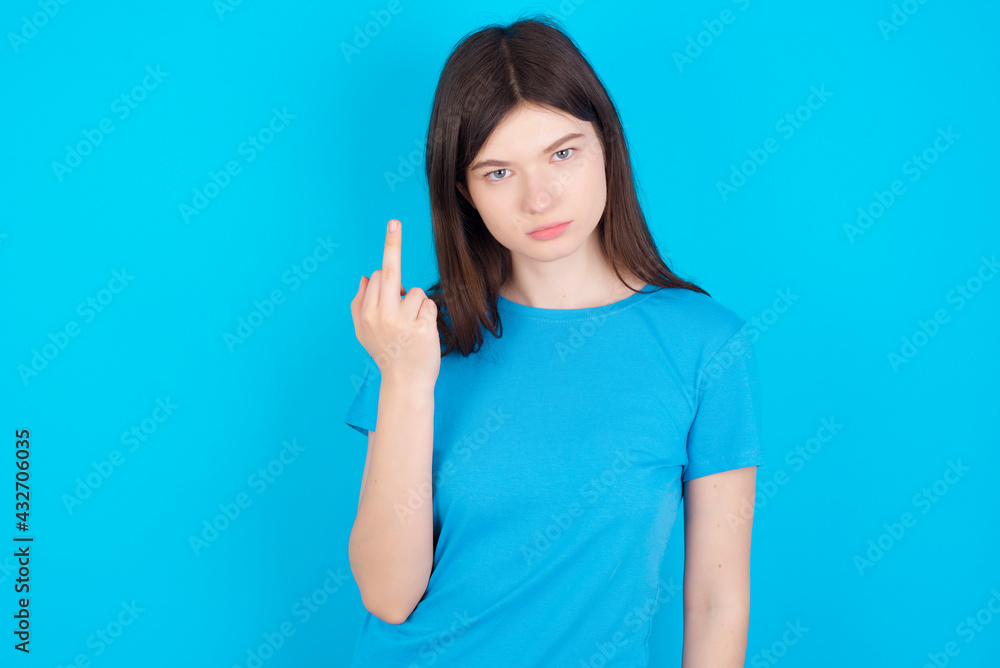 Fototapeta premium young beautiful Caucasian woman wearing blue T-shirt over blue wall shows middle finger bad sign asks not to bother. Provocation and rude attitude.