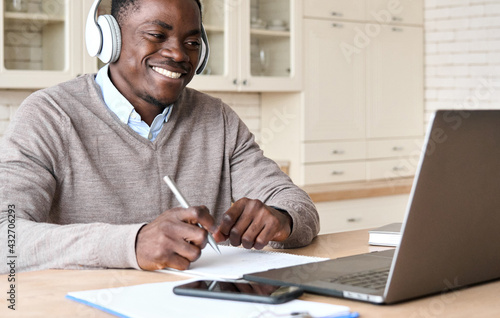 Adult happy smiling African American black male student wearing headphone sit at kitchen table, watching online video conference learning virtual course teaching using laptop computer in homeoffice.