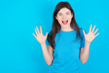 Delighted positive young beautiful Caucasian woman wearing blue T-shirt over blue wall opens mouth  and arms palms up after having great result