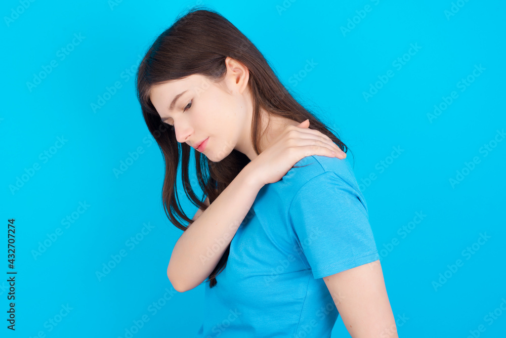 young beautiful Caucasian woman wearing blue T-shirt over blue wall got back pain