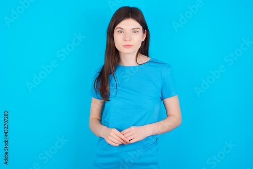 Photo of cheerful confident young beautiful Caucasian woman wearing blue T-shirt over blue wall arms together © Jihan