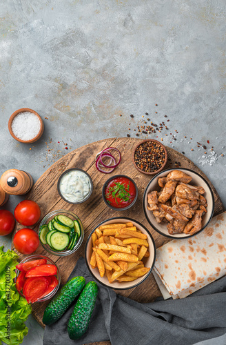 Fried meat, potatoes, vegetables and pita bread on a gray background.