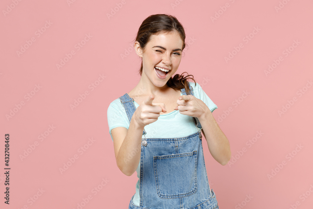 Young friendly smiling happy leader caucasian woman 20s wear denim clothes blue t-shirt point index finger camera on you isolated on pastel pink background studio portrait. People lifestyle concept Young friendly smiling happy leader caucasian woman 20s wear denim clothes blue t-shirt point index finger camera on you isolated on pastel pink background studio portrait. People lifestyle concept