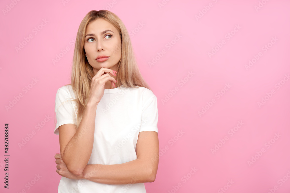 Pensive young woman holding chin in doubt portrait. thinking creative person in white shirt, dreamy girl thought and looking up isolated on pink studio background Pensive young woman holding chin in doubt portrait. thinking creative person in white shirt, dreamy girl thought and looking up isolated on pink studio background