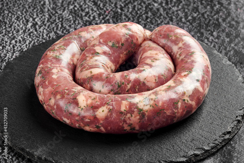 raw sausage in a round shape for grilling or roasting on a black stone background